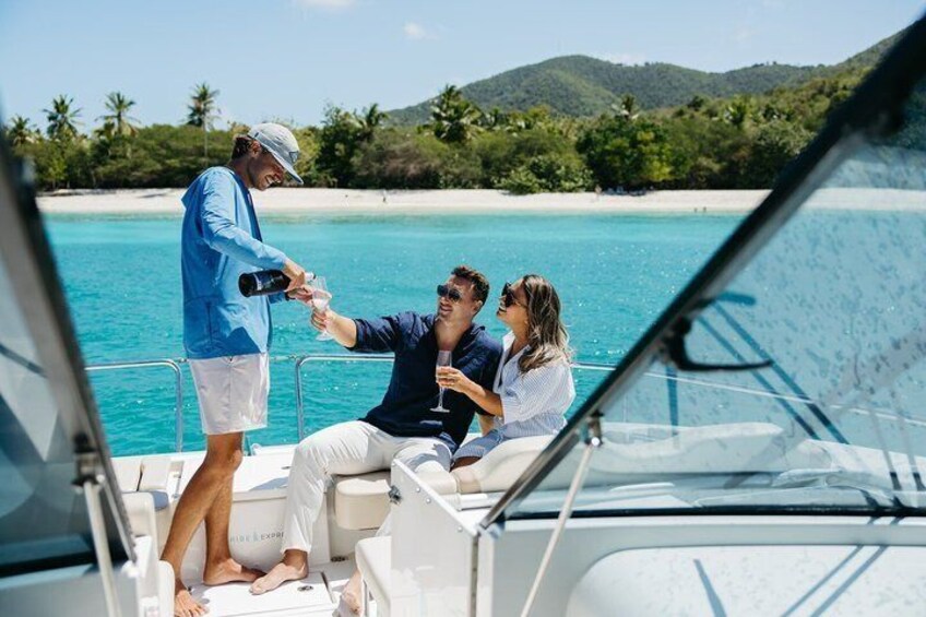 A person pouring a drink on a boat with a tropical beach and mountains in the background. 1