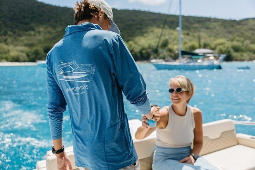 A person in a blue boat with a logo, another person in a white tank top, and a calm body of water with boats in the background. 3