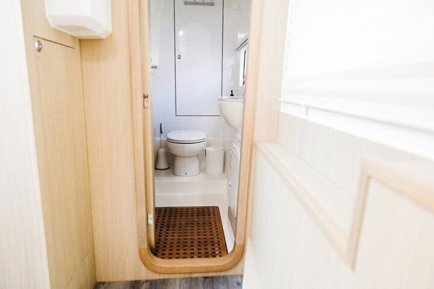 A narrow bathroom with a toilet, sink, and shower. 2