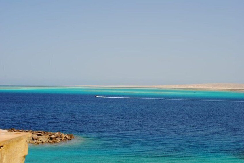 A calm sea with a clear horizon, a boat in the distance, and a rocky coastline. 3