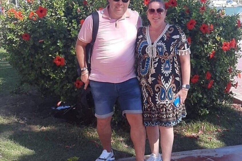 Two people standing in front of a bush with red flowers. 5