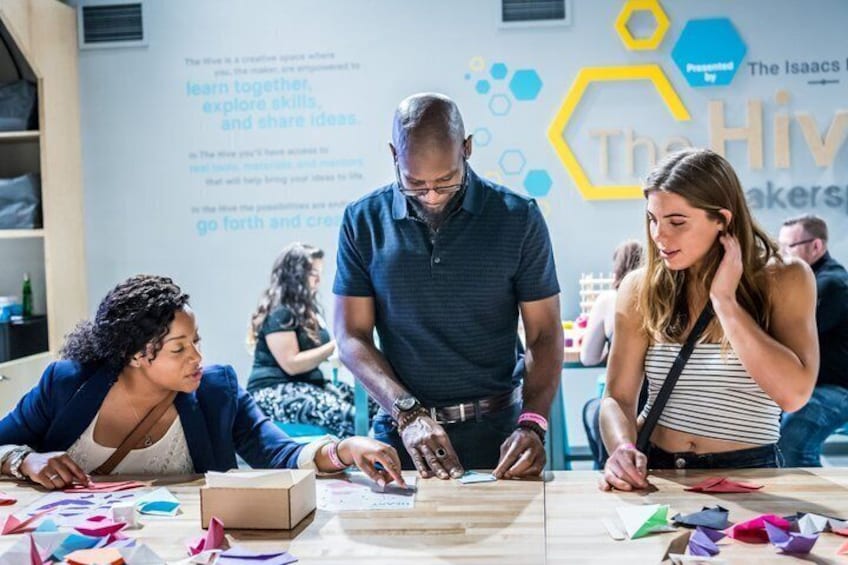 A group of people engaged in a collaborative activity at a table with papers and a box, in a room with a hexagonal wall design. 5