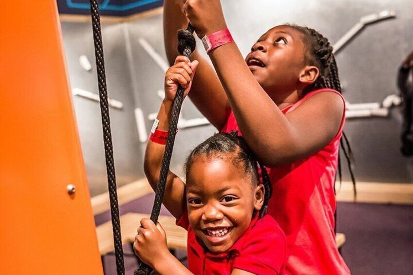 Two children in red shirts using a rope climbing apparatus in a gym. 4
