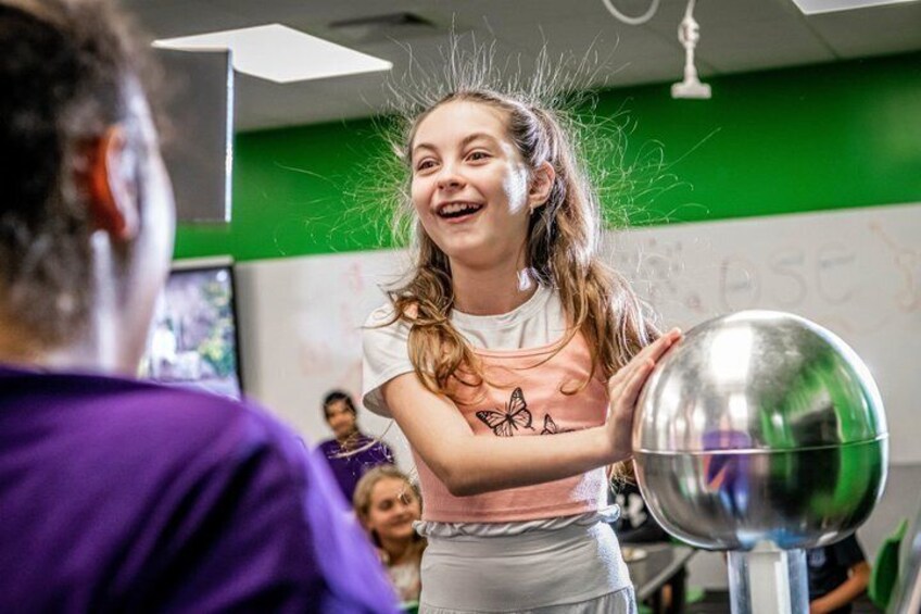 A person in a classroom with a green wall and a whiteboard, holding a metallic object. 2