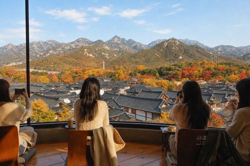 Three people sitting by a window overlooking a mountainous landscape with traditional buildings. 1