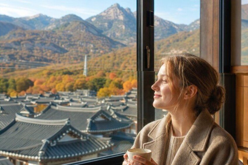 A person holding a cup, looking out at a traditional building with a mountainous landscape in the background. 4