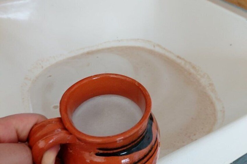 A hand holding a red ceramic mug with a handle, partially submerged in a white ceramic sink. 2