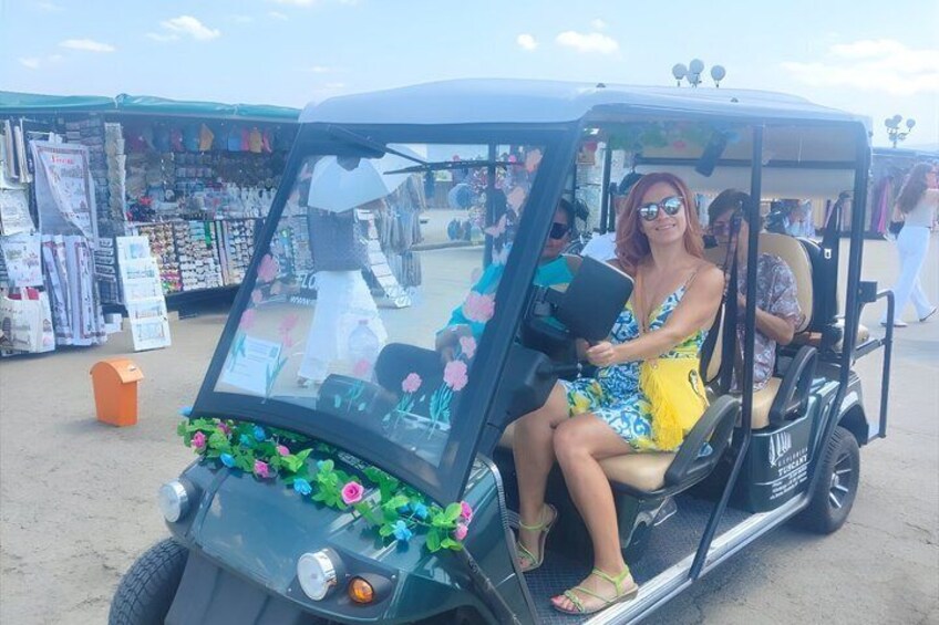 A woman in a yellow dress sitting in a golf cart at a market. 1