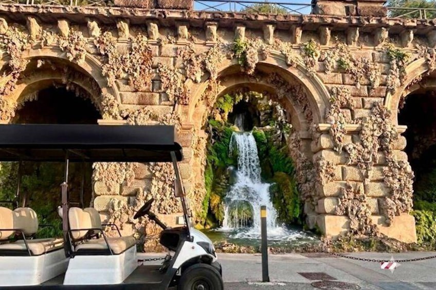 A stone bridge with a waterfall, a golf cart, and a paved walkway. 2