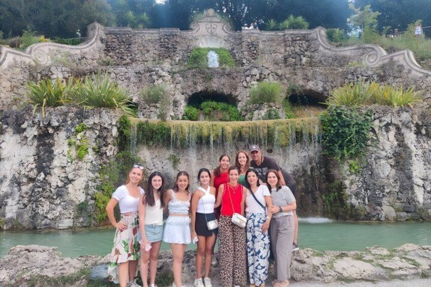 A group of people standing in front of a stone bridge with a waterfall. 1