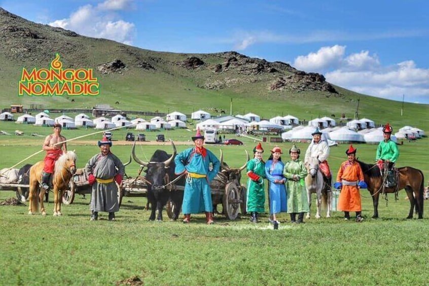 A group of people in traditional attire standing in a grassy field with yurts in the background. 1