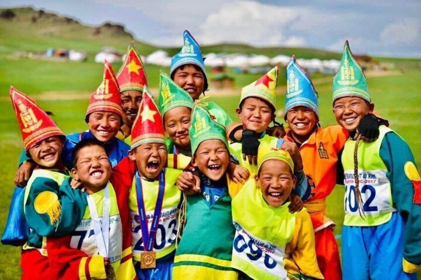 A group of children wearing colorful hats and vests, standing in a grassy field. 4