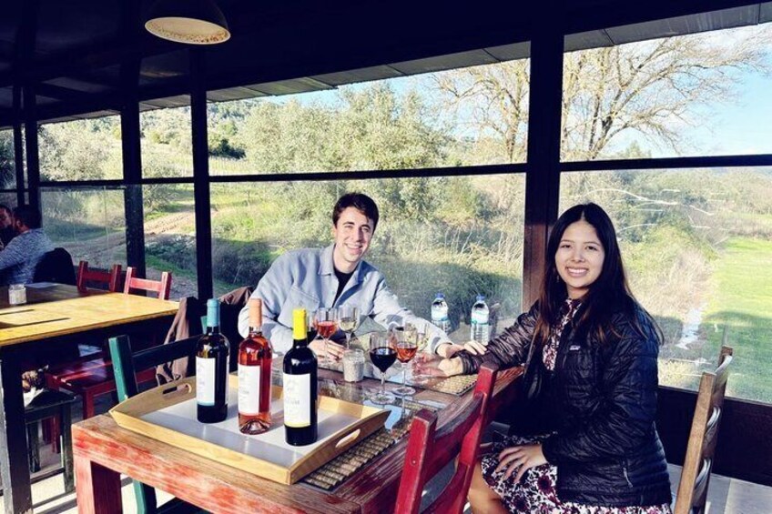 Two people seated at a table with wine bottles and glasses, overlooking a scenic outdoor view. 3