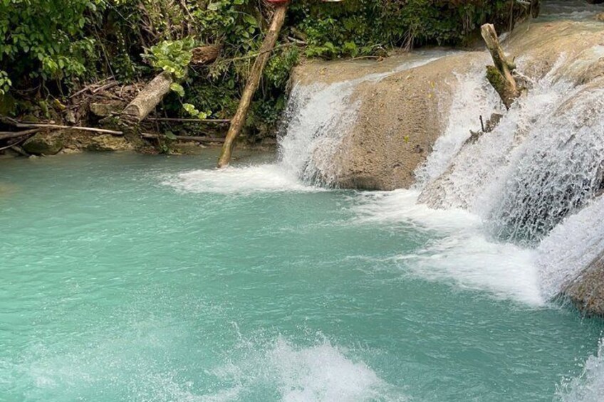 A turquoise waterfall cascading over rocks in a forested area. 5