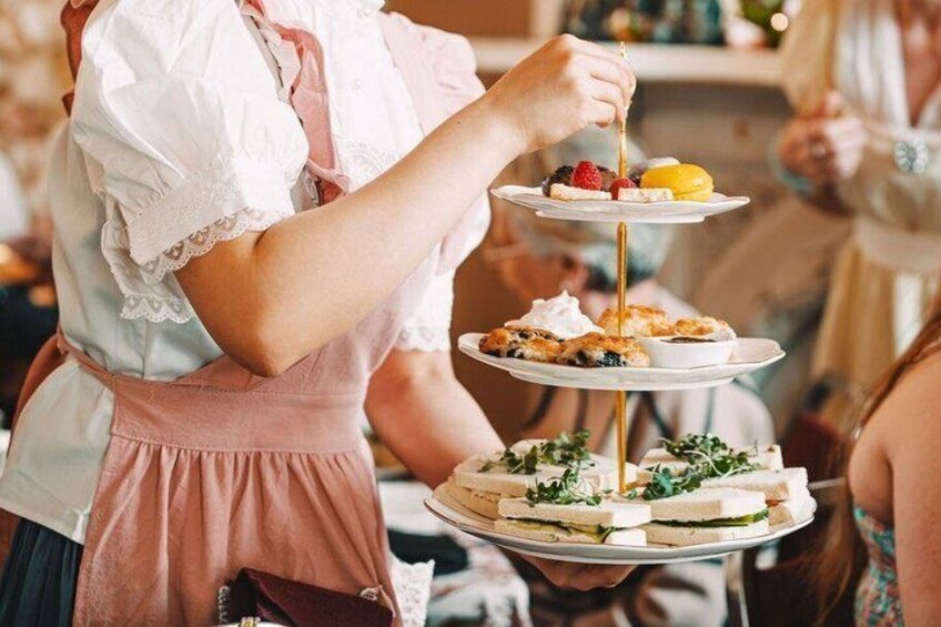 A person serving a multi-tiered tray with sandwiches and fruits. 3