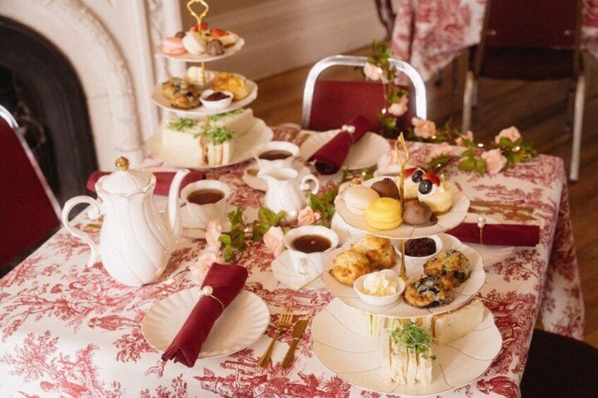 A table set for a tea party with a tiered dessert stand, teapots, and floral decorations. 1