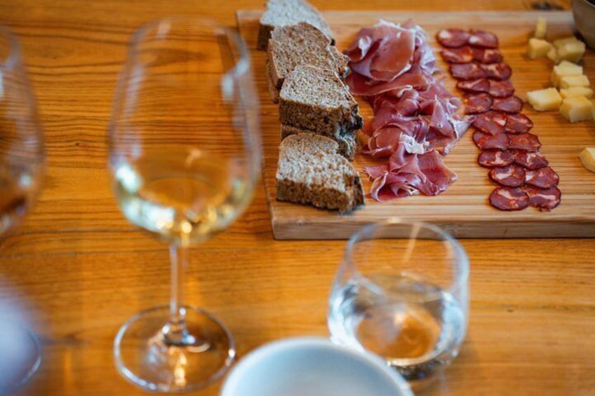 A wooden table with sliced meats, cheese, and bread, accompanied by wine glasses. 2