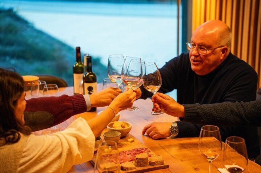 A person toasting with a wine glass at a table with a bottle of wine and a dessert plate. 1