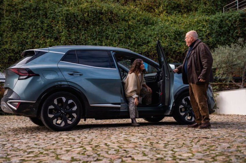 A blue SUV parked on a cobblestone surface with a man and a woman standing beside it. 5