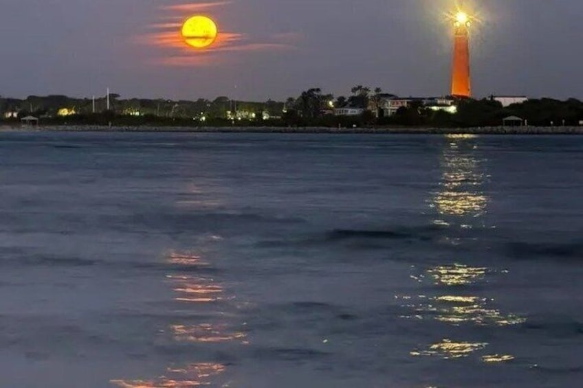 A sunset over water with a lighthouse and buildings in the background. 1