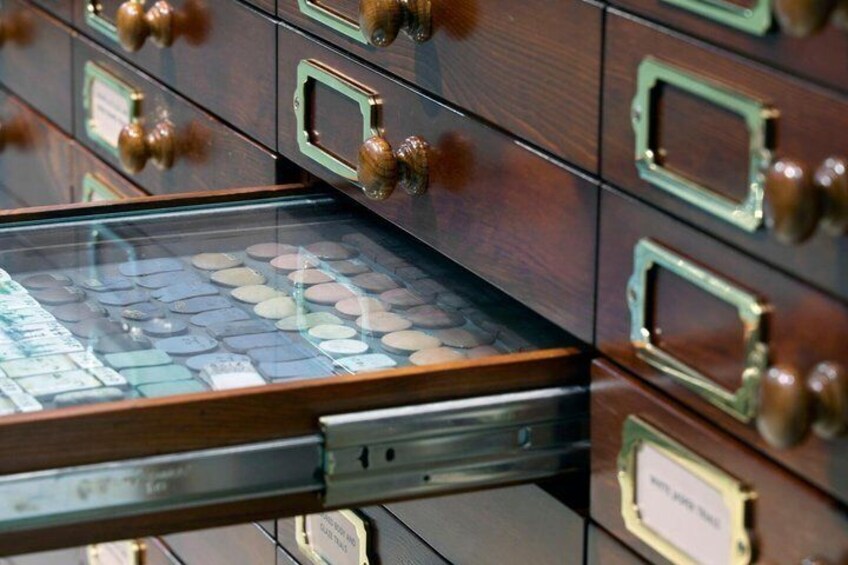 A collection of wooden drawers with brass handles and a glass display case containing coins. 3