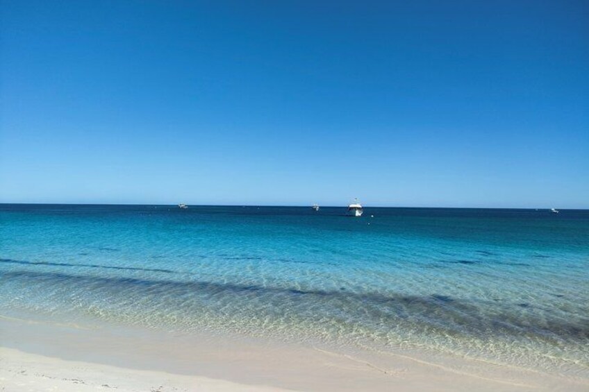 A clear blue sea, a sandy beach, and a distant boat. 1