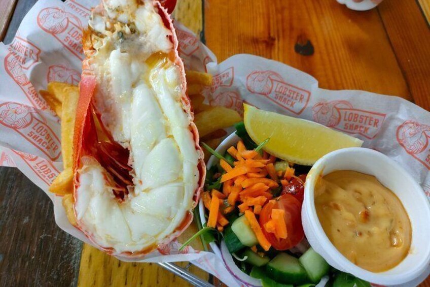 A lobster tail, fries, salad, and dipping sauce on a wooden table. 3