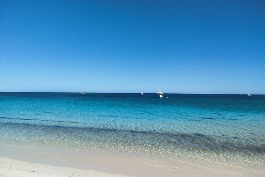 A beach with clear turquoise water, a sandy shore, and a lighthouse in the distance. 3