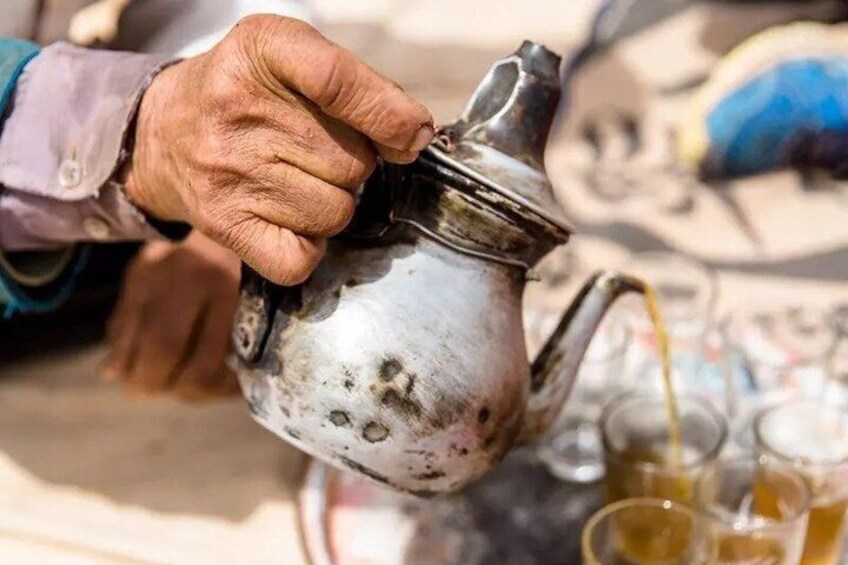 A hand pouring liquid from a tarnished metal jug into a glass. 3