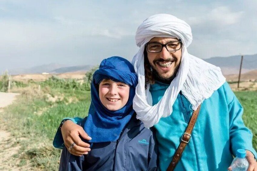 Two people in traditional attire standing on a grassy field with a mountainous backdrop. 5