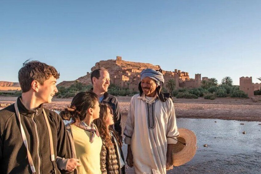 A group of people standing by a river with a historic fort in the background. 1