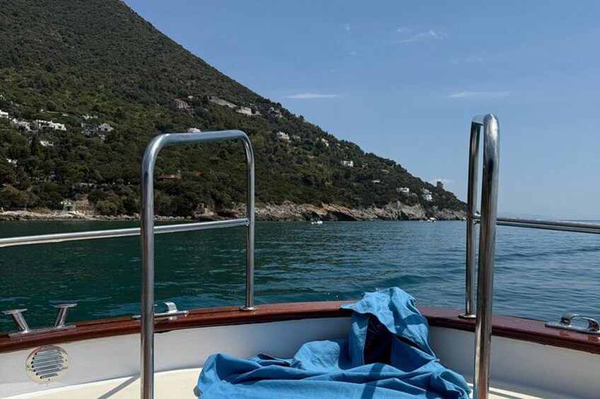 A boat with metal railings, a blue cloth, and a mountainous coastline in the background. 5