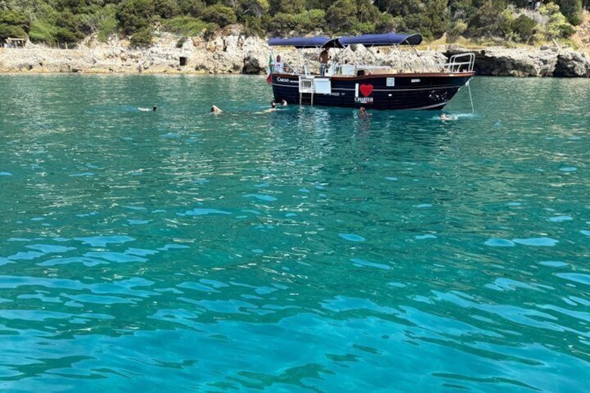 A boat named 'Chameleon' on calm turquoise waters with swimmers in the background and rocky terrain along the shore. 4