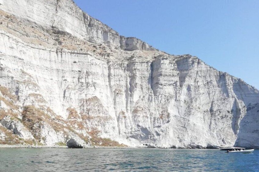 A white cliff by a body of water with a boat. 1