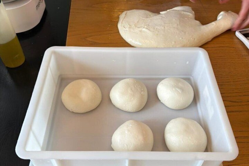 A white container with five round dough balls on a wooden table. 5