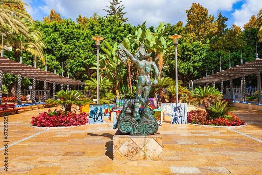A statue of a figure with a raised arm, surrounded by a garden with various plants and flowers. 3
