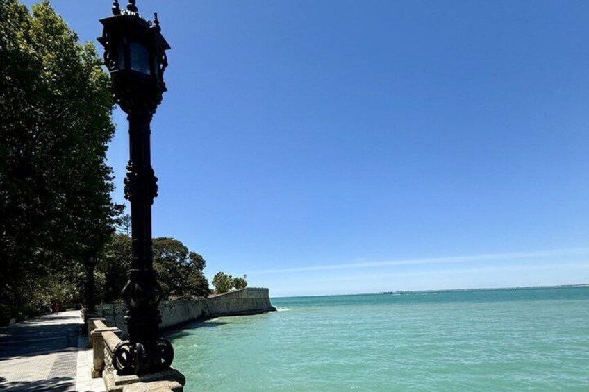 A coastal walkway with a black lamppost, clear blue sea, and a stone wall. 5