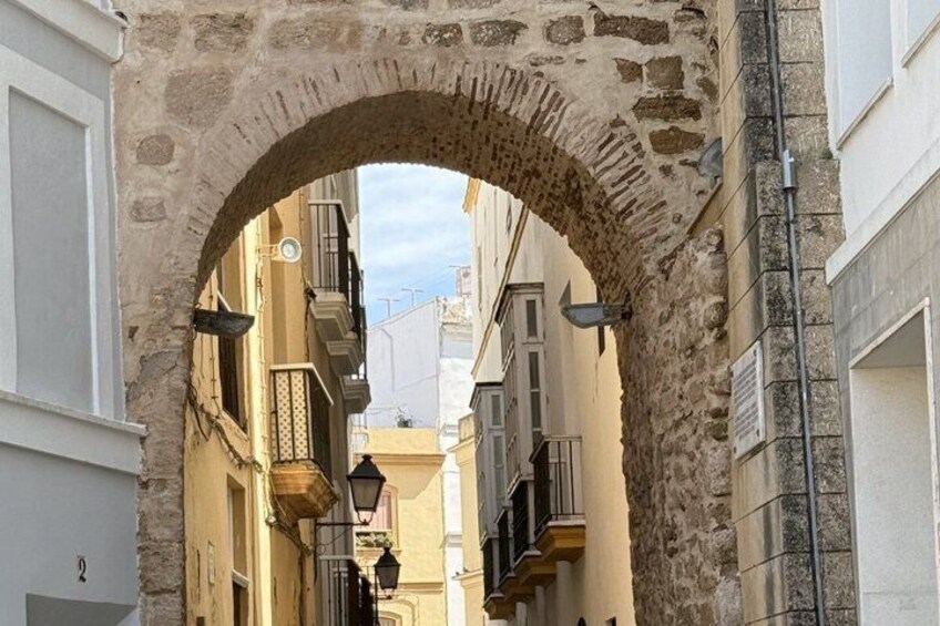 An arched stone gateway between buildings with balconies and a clear sky. 4