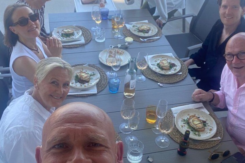 A group of people dining at an outdoor table with plates of food and glasses of wine. 3