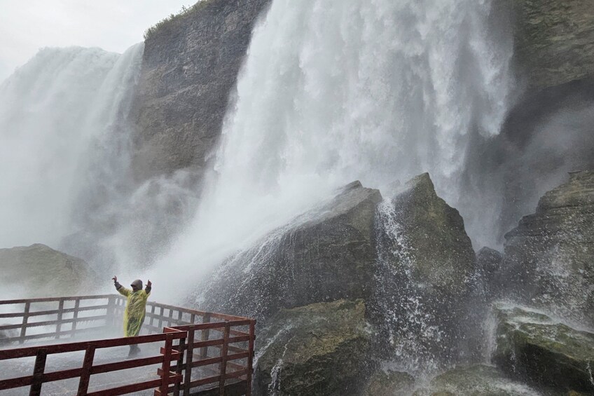 A person in a yellow raincoat standing on a platform with a waterfall in the background. 3