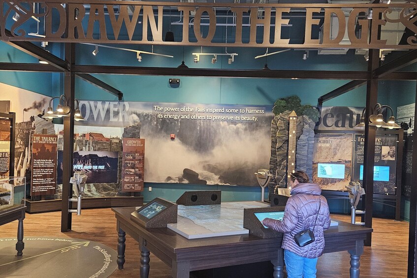 An indoor exhibit with a sign reading 'Drawn to the Edge' and a large poster about the power of the falls. 5