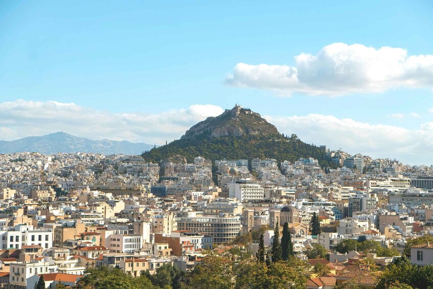 A cityscape with a prominent hilltop, dense urban buildings, and a clear sky. 2