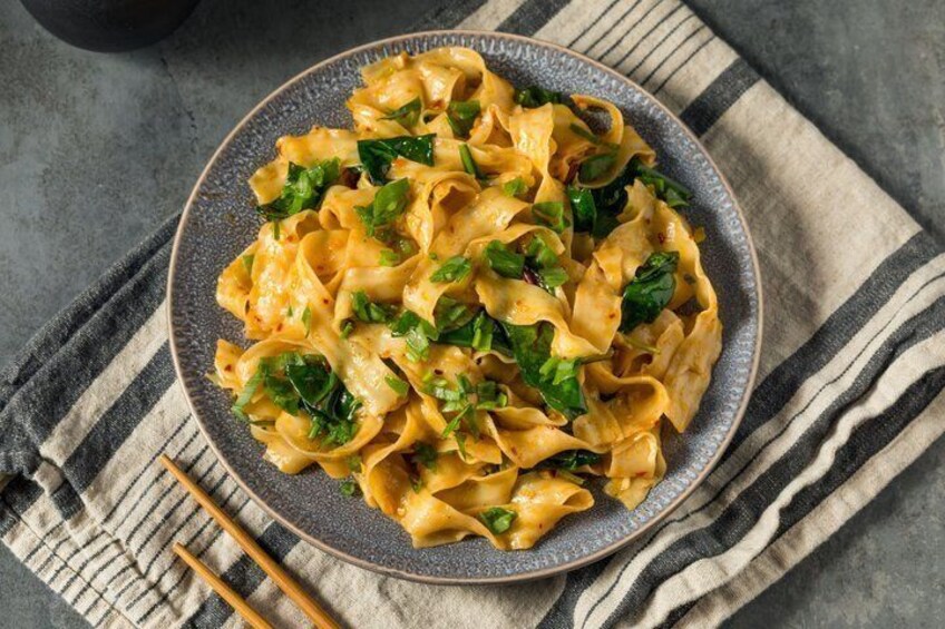 A plate of pasta with a creamy sauce and chopped greens, placed on a striped cloth. 1