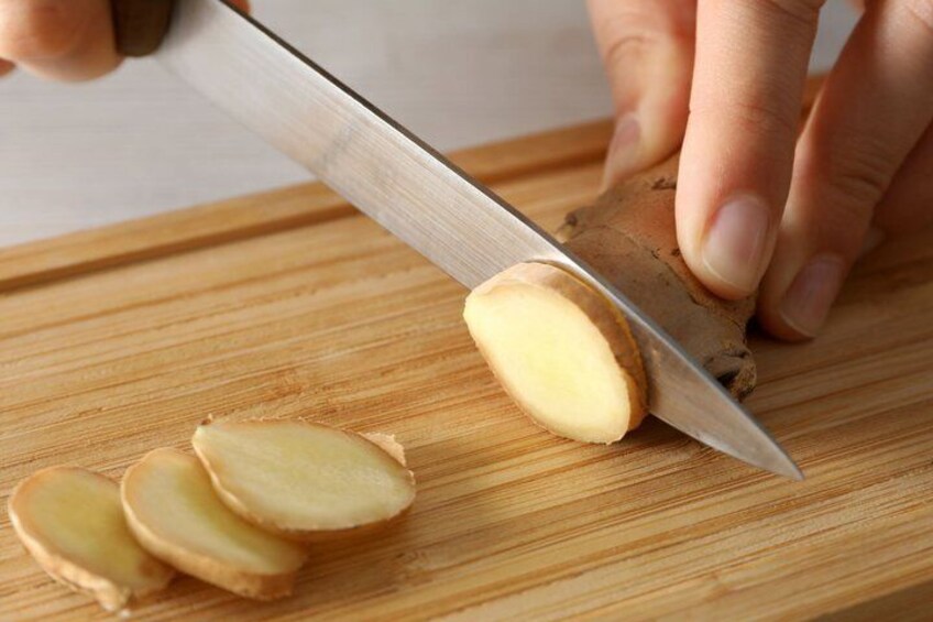 A person slicing ginger on a wooden cutting board. 5