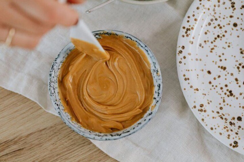 A bowl of peanut butter with a spoon, on a cloth, next to a plate with coffee stains. 3