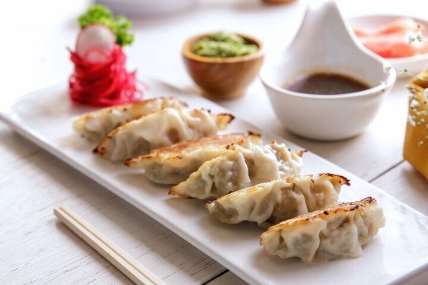 A plate of pan-fried dumplings with dipping sauce and pickled vegetables. 3