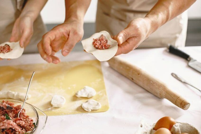 Hands preparing dumplings with a bowl of filling and a cutting board. 1