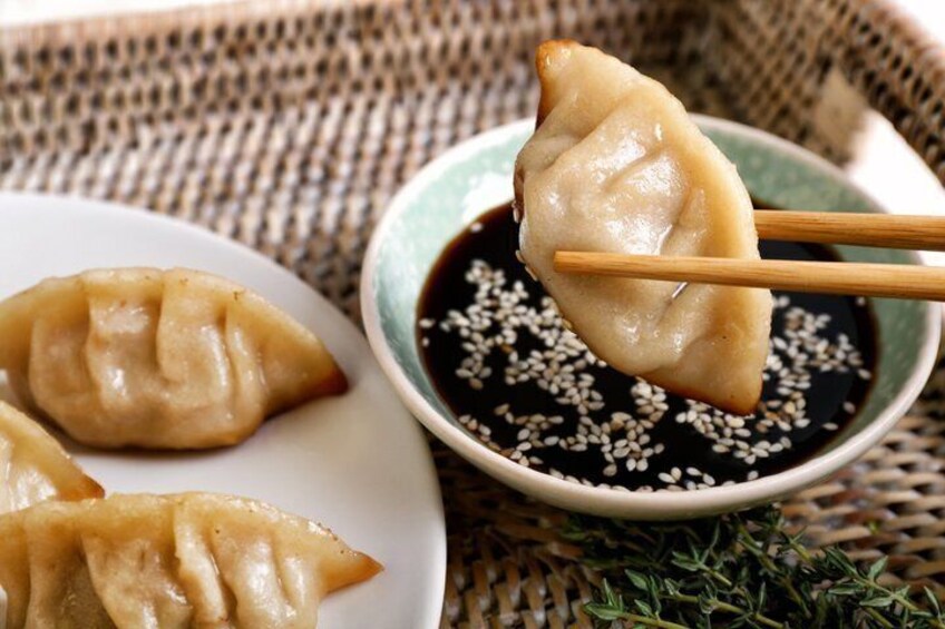 A plate of dumplings with a dipping sauce and sesame seeds. 4