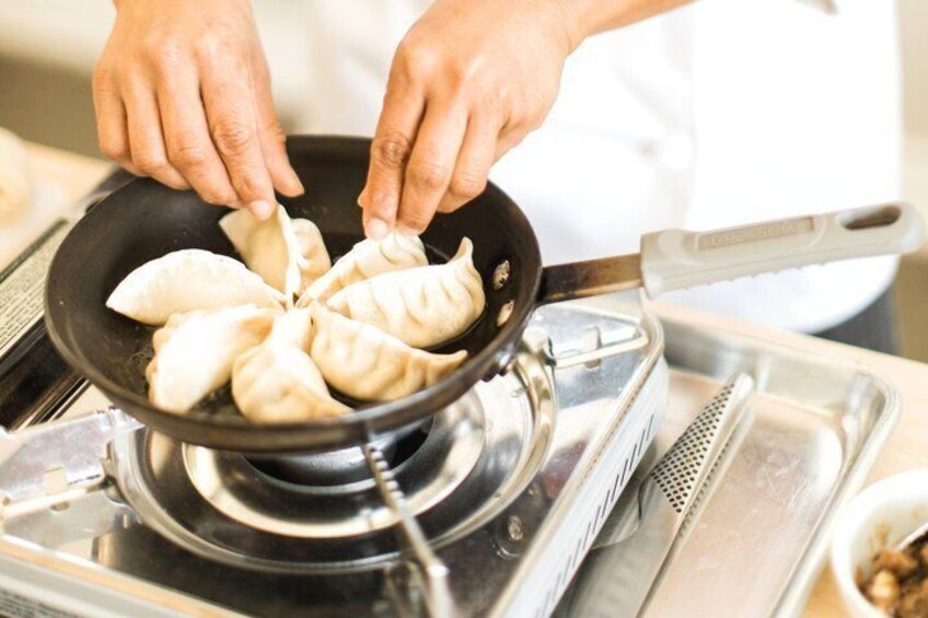 A person cooking dumplings in a pan on a stove. 5