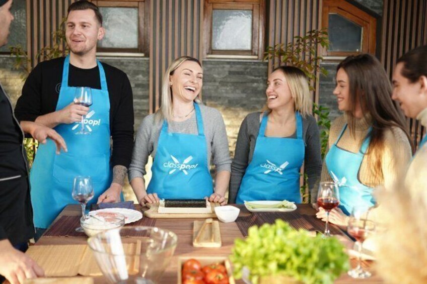 A group of people wearing blue aprons, engaged in a cooking activity with ingredients and cooking utensils on a wooden table. 2